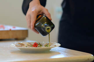 Chef pouring extra virgin olive oil on plated fish.
